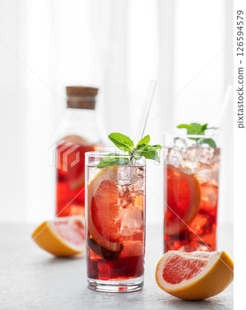 Two glasses of cocktail with grapefruit, mint and ice on a table against a window with natural light 126594579