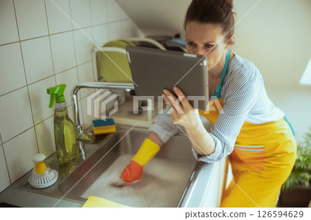 Distracted Woman Cleans Sink with Tablet Distracted Woman Cleans Sink with Tablet 126594629