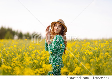 Young woman walking flowering field gently touch yellow flowers. Summer landscape. 126595447