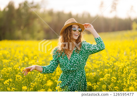 Beautiful woman in bright dress and elegant hat walks and has fun in rapeseed field. Nature, rest. 126595477
