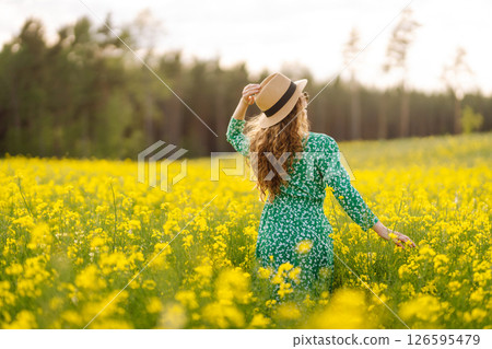 Beautiful woman in bright dress and elegant hat walks and has fun in rapeseed field. Nature, rest. 126595479