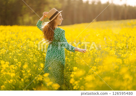 Young woman walking flowering field gently touch yellow flowers. Summer landscape. 126595480
