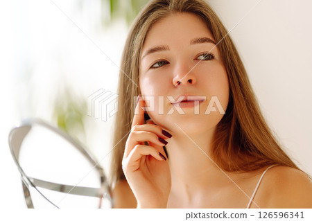 A beautiful woman looking in mirror, examines acne, pigmentation. Cosmetic care. Allergic reaction. 126596341