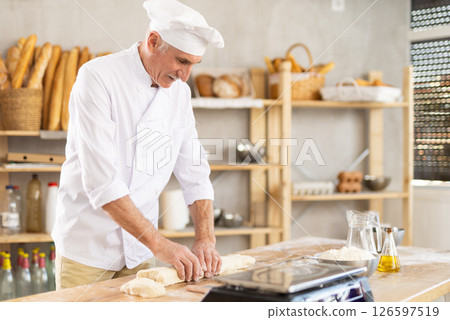 Elderly man baker rolls out dough 126597519