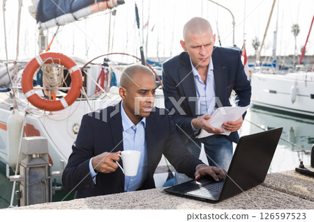 Men in suits verifying documentation on a laptop in the seaport Men in suits verifying documentation on a laptop in the seaport 126597523