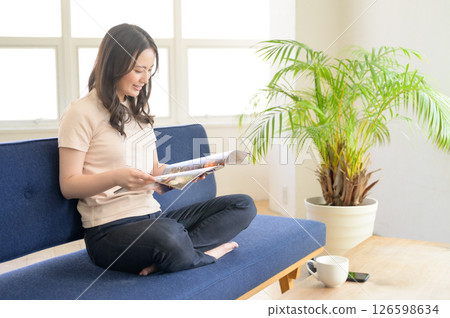 A woman sitting on a sofa in the living room looking at a pamphlet 126598634