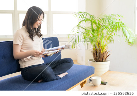 一位女士坐在客廳的沙發上看一本小冊子 一位女士坐在客廳的沙發上看一本小冊子 126598636