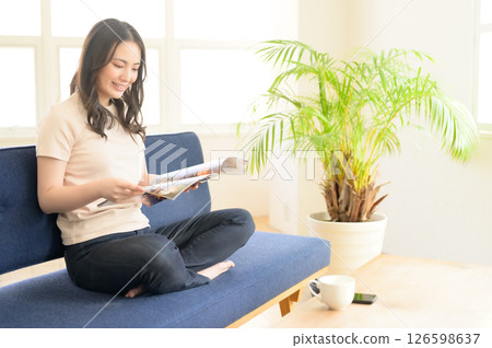 一位女士坐在客廳的沙發上看一本小冊子 一位女士坐在客廳的沙發上看一本小冊子 126598637