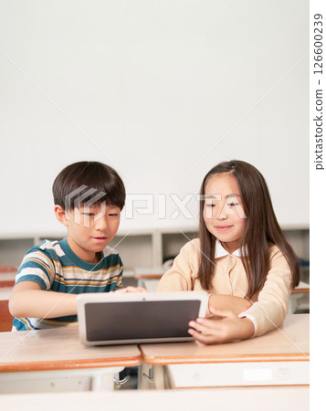 Elementary school boys and girls looking at tablet screens together 126600239