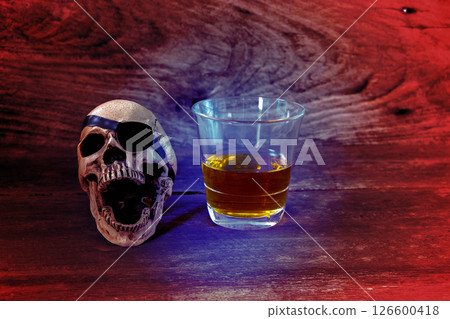 The pirate skull with a glass of rum liquor on brown wooden background. The pirate skull with a glass of rum liquor on brown wooden background. 126600418