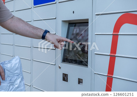 Customer hand touching touchscreen interface on automated parcel locker operating system for modern self-service package access 126601251