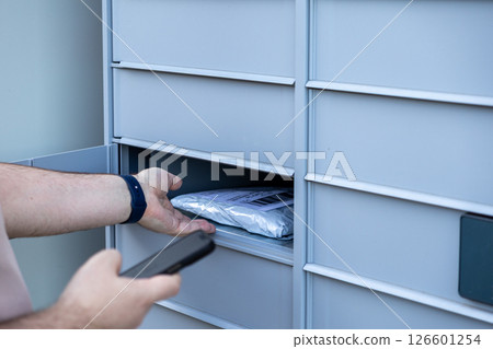 Customer hand retrieving package from open compartment of automated parcel locker illustrating modern e-commerce self-service delivery 126601254