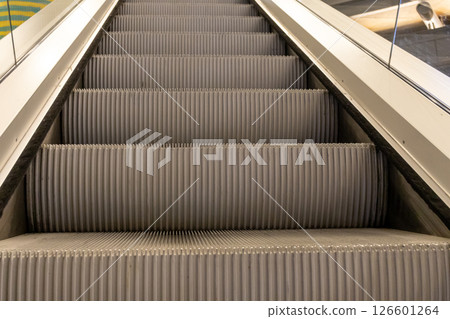 Ribbed metal steps of escalator moving upwards provide vertical transportation in indoor public building facilitating movement between floors 126601264