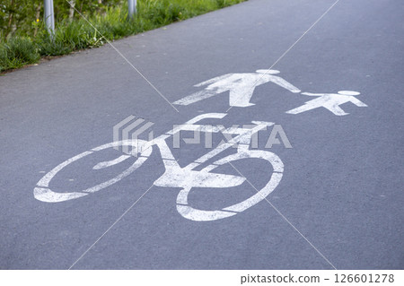Painted bicycle and pedestrian icons on asphalt path indicate shared use for cyclists and people walking including children Painted bicycle and pedestrian icons on asphalt path indicate shared use for cyclists and people walking including children 126601278