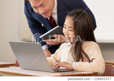 Elementary school student using a PC and a teacher instructing 126601477