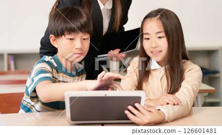 Elementary school boys and girls looking at tablet screens together 126601481