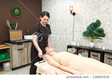 A female massage therapist gently begins a forehead massage on a lying client of the salon A female massage therapist gently begins a forehead massage on a lying client of the salon 126601616