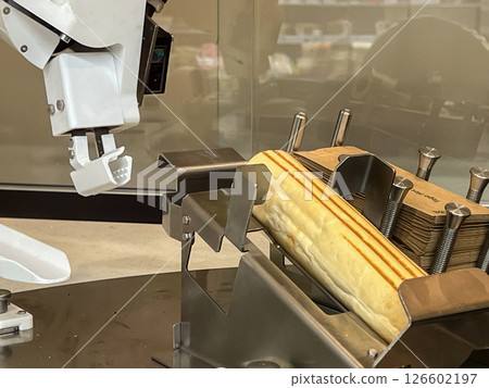 White robotic arm grips panini in metal holder showing automation in food preparation near paper bags displaying Super Hot text within modern food service technology 126602197