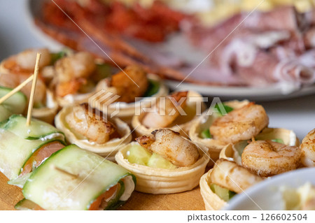 gourmet shrimp tartlets and cucumber salmon rolls on a wooden board, served as festive appetizers 126602504