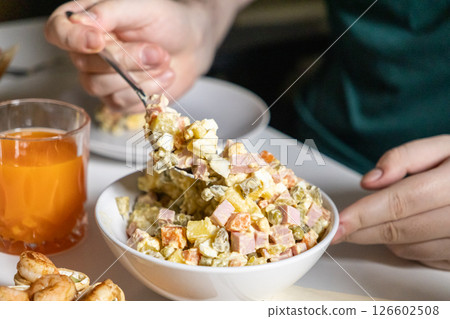 person scooping Olivier salad from a bowl, creamy texture with diced ham, potatoes, carrots, pickles, and mayonnaise dressing 126602508