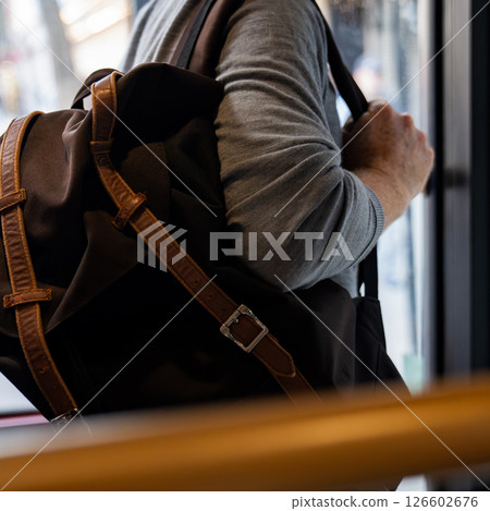 A person holding a brown backpack, getting off a bus while gripping the door handle. The image captures the typical commuter moment in an urban setting 126602676