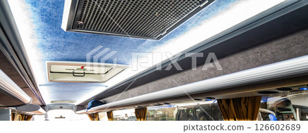 Ceiling area and overhead storage compartments of a modern tour bus are shown, with lighting panels and air vents visible. Bag is placed in the open storage space above the passenger seats. Ceiling area and overhead storage compartments of a modern tour bus are shown, with lighting panels and air vents visible. Bag is placed in the open storage space above the passenger seats. 126602689