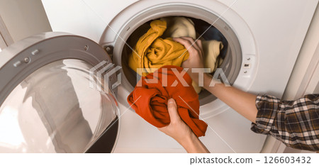 Woman puts bright clothes into a washing machine. Woman puts bright clothes into a washing machine. 126603432
