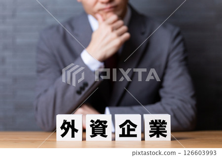 A middle-aged male businessman wearing a suit and worrying about a foreign company block 126603993