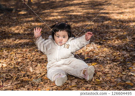 [一名 1 歲的孩子坐在覆蓋著落葉的冬季公園裡玩耍] 126604495