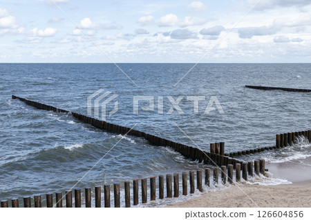 View of wooden breakwaters extending into the ocean, with gentle waves View of wooden breakwaters extending into the ocean, with gentle waves 126604856