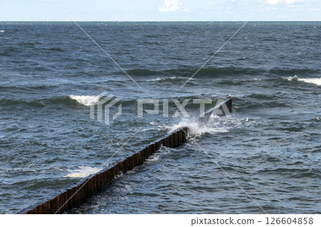 Dynamic image showcasing ocean waves striking a wooden breakwater 126604858