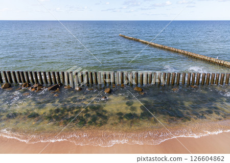A scenic view of a wooden breakwater extending into the calm sea 126604862