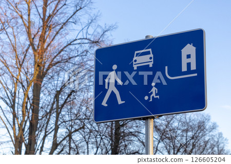 Residential zone traffic sign with symbols of pedestrian, child playing with a ball, car, and house against a blue background, indicating mixed-use area safety 126605204