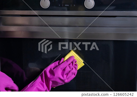 hand in pink gloves cleaning oven door with yellow sponge for a spotless kitchen surface 126605242