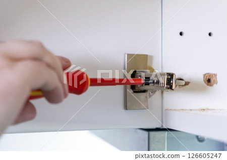 Adjusting a cabinet hinge with a screwdriver for precise door alignment and secure mounting Adjusting a cabinet hinge with a screwdriver for precise door alignment and secure mounting 126605247