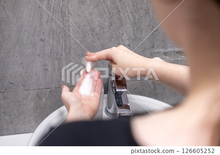 applying liquid soap on hands before washing under running water in a bathroom sink 126605252