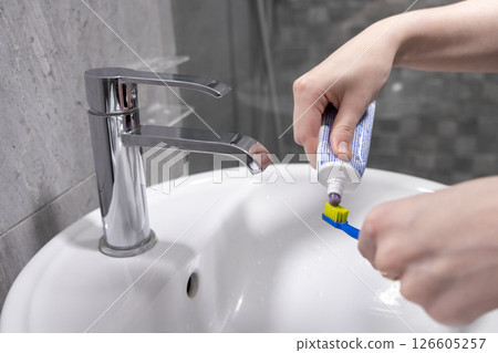 Squeezing toothpaste onto a toothbrush over a white sink in a bathroom hygiene routine 126605257