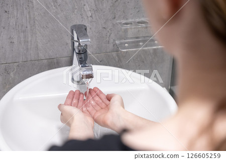 Person washing hands under running water from a modern bathroom faucet for hygiene and cleanliness Person washing hands under running water from a modern bathroom faucet for hygiene and cleanliness 126605259
