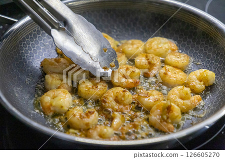 Shrimp frying in a pan with tongs stirring, sizzling in oil and spices for a flavorful seafood dish Shrimp frying in a pan with tongs stirring, sizzling in oil and spices for a flavorful seafood dish 126605270
