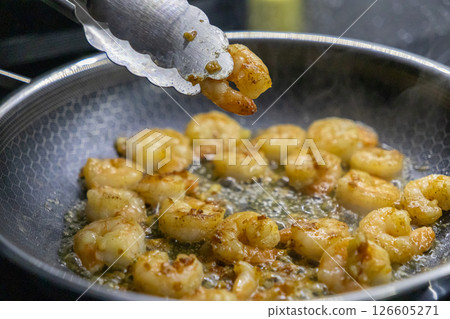 Cooked shrimp being held by tongs above a sizzling frying pan filled with golden, crispy seafood Cooked shrimp being held by tongs above a sizzling frying pan filled with golden, crispy seafood 126605271