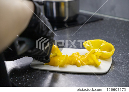 chopping yellow bell pepper on cutting board with gloved hand in kitchen setting, preparing fresh vegetables 126605273