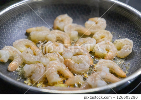 raw shrimp sizzling in frying pan with oil and seasoning during cooking process on stovetop 126605280