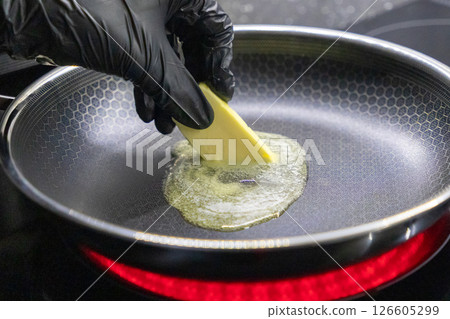 hand in black glove melting butter in frying pan on hot stovetop hand in black glove melting butter in frying pan on hot stovetop 126605299