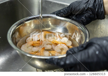fresh shrimp being rinsed in stainless steel bowl under running water by hands in black gloves in kitchen sink fresh shrimp being rinsed in stainless steel bowl under running water by hands in black gloves in kitchen sink 126605313