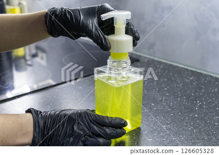 hands in black gloves holding transparent soap dispenser with yellow liquid soap on a kitchen countertop, hygiene concept hands in black gloves holding transparent soap dispenser with yellow liquid soap on a kitchen countertop, hygiene concept 126605328