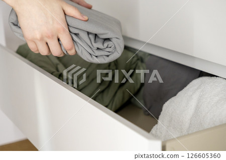 organizing gray bedsheet into drawer by hand with green and white fabrics neatly arranged for clean home storage solution 126605360