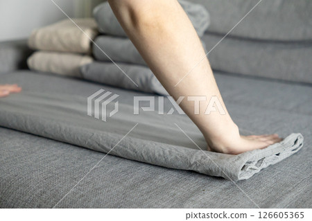 smoothing gray bedsheet by hand on soft fabric surface with neatly folded linens stacked in background for tidy home organization smoothing gray bedsheet by hand on soft fabric surface with neatly folded linens stacked in background for tidy home organization 126605365