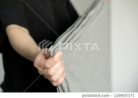 holding neatly folded gray linen fabric with clean hands against simple white background for minimal and organized home aesthetic 126605371