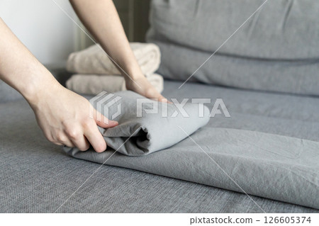 folding gray linen fabric on a soft gray sofa with neatly arranged towels in the background for a cozy and organized home atmosphere folding gray linen fabric on a soft gray sofa with neatly arranged towels in the background for a cozy and organized home atmosphere 126605374