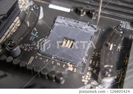 cpu socket on a motherboard with visible pins and fastening brackets during computer assembly process, close-up detail of electronic components 126605424